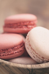 closeup shot of pastel colored macarons with strawberry and rose flavour in wood bowl, vintage toned photo