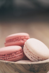 closeup shot of pastel colored macarons with strawberry and rose flavour in wood bowl, vintage toned photo