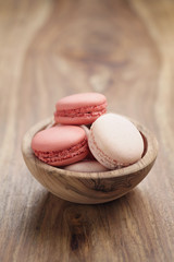 pastel colored macarons with strawberry and rose flavour in wood bowl on table