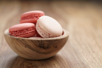 pastel colored macarons with strawberry and rose flavour in wood bowl on table
