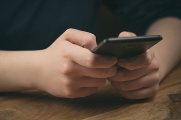 young female teen hands using smatphone sitting at the table closeup, shallow focus