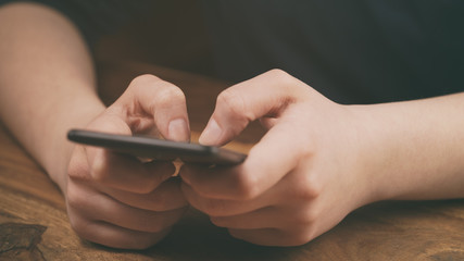 young female teen hands using smatphone sitting at the table closeup, shallow focus