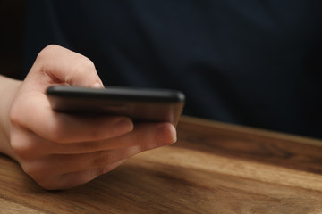 young female teen hand using smatphone sitting at the table closeup, shallow focus with copy space