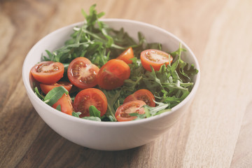 cherry tomatoes with arugula salad in white bowl on wooden table, vintage toned photo