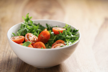 cherry tomatoes with arugula salad in white bowl on wooden table