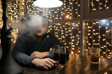 man smoking pipe of hookah in night cafe