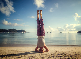 Young attractive man doing yoga on the beach at dawn, standing on his head