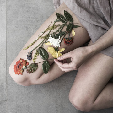 Woman arranging dried flattened flowers on her leg