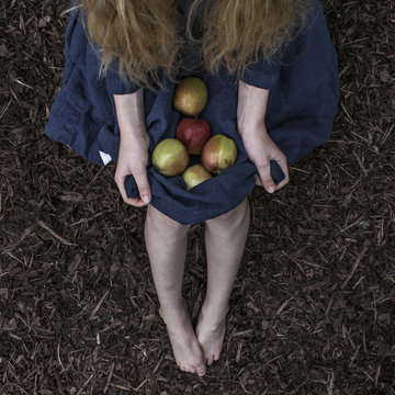 Young girl sitting outdoors with apples on her lap
