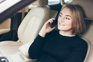 Close-up portrait of beautiful happy and laughing with all teeth young Caucasian woman is sitting in car and talking on mobile phone. Lifestyle, traveling and communication concept.