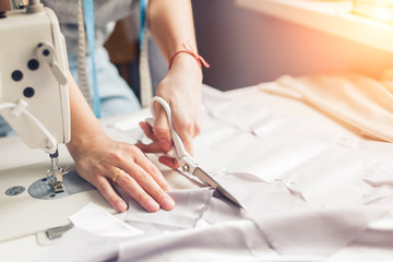 pattern, scissors, tape measure, and a sewing machine. Workplace of seamstress. Dressmaker cuts dress detail on the sketch lines. - obrazy, fototapety, plakaty
