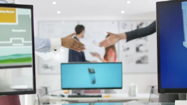  Workers at technology design co. shake hands, with other colleagues working