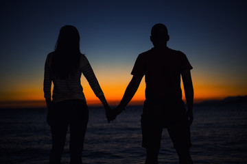 Young couple in love looking at the sunset at the seaside