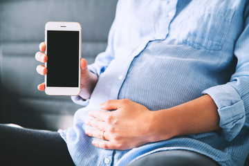 Pregnant woman holding and showing mobile phone with empty display.