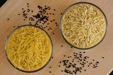 Noodles and orzo in glass bowls on chopping board