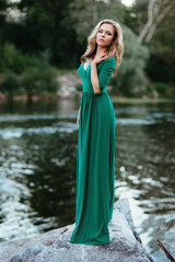 Beautiful girl posing on rocks near the water. Model in a green dress in nature.