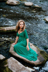 Beautiful girl posing on rocks near the water. Model in a green dress in nature.