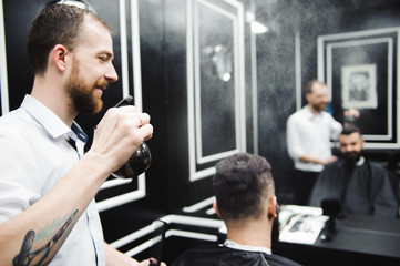 Naklejka na ściany i meble Young handsome barber making haircut of attractive man in barbershop