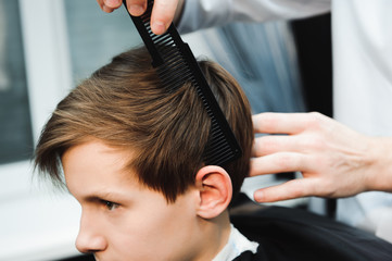 Young handsome barber making haircut of cute boy in barbershop