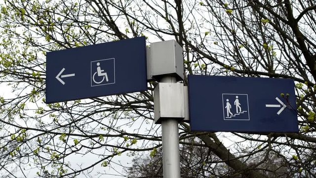 Two signs showing different access directions for able bodied stair access and special needs handicapped ramp access locations.