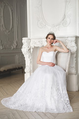 Fototapeta premium Beautiful bride posing in wedding dress in a white photo Studio. Mirror. Sofa. Bouquet. The door. Chandelier.