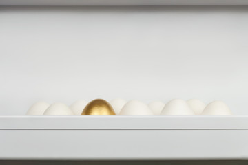 Ten chicken eggs on the shelf of the kitchen refrigerator with one golden egg.