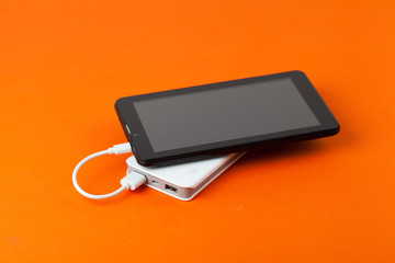 Tablet PC and power bank isolated on orange background. Top view.