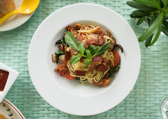 Delicious dish, pasta stir-fry with bacon, dry chilli, garlic, tamato, basil and young green peppercorns, in white plate on green background