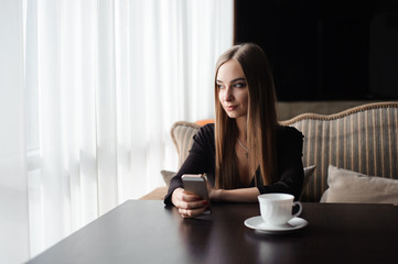 Young attractive girl sitting alone near big window in coffee shop during free time