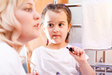 Happy loving family. Mother and daughter are doing makeup and having fun. Mother and daughter sitting at dressing table and looking at the mirror.