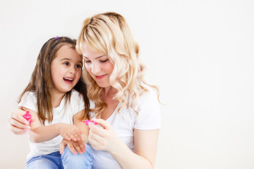 Mom and daughter in the bedroom on the bed in the curlers make up, paint their nails and have fun