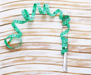 Diet concept - fork with measuring tape on a wooden table