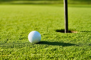 Golf ball on the green grass near to pitch.