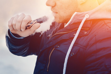 Close-up A man vape smokes an electronic cigarette against the sunset. The steam is falling. Concept rejection of cigarettes. high contrast and monochrome color tone.