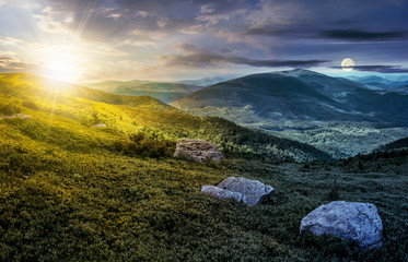 day and night time change concept image. huge stones among the grass on top of the hillside meadow near the edge of a mountain. vivid summer landscape.