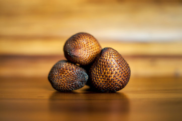 Three ripe whole salak or shake fruits lying on wooden background. Exotic fruits