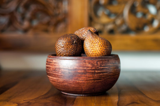 Brown wooden bowl with salak or snake fruits. Carving wooden background. Exotic fruits from Bali, Indonesia