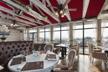 spacious restaurant with large panoramic windows, a leather sofa, elegant chairs and a red ceiling - obrazy, fototapety, plakaty