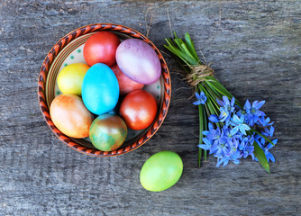 Painted eggs in a ceramic bowl and a bouquet of spring blue flowers on a wooden table.