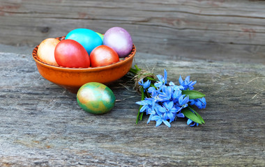 Easter composition.Painted eggs in a ceramic bowl and a bouquet of spring blue flowers on a wooden table.