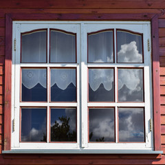 Window in country wooden house in Russia with curtains and reflections of blue sky in summer.
