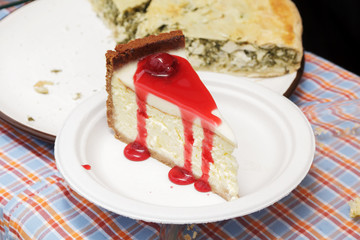Slice of cheesecake topped with cherry compote on plate on brown table with dessert, top view