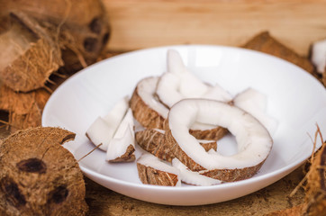 Chopped coconut in a white plate on a wooden background.