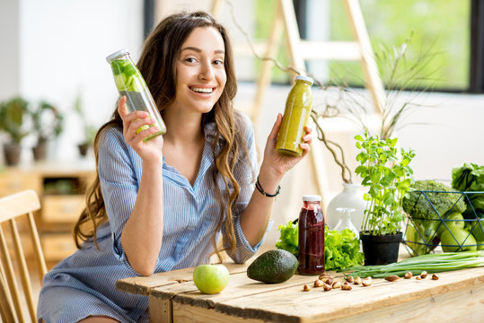 Beautiful woman sitting with healthy green food and drinks at home. Vegan meal and detox concept