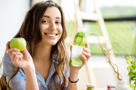 Beautiful happy woman sitting with drinks and healthy green food at home. Vegan meal and detox concept