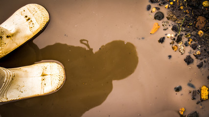 Reflection in a puddle of a child standing in white rubber boots.