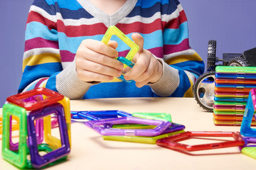 Boy is building with colorful magnetic construction set. Close u