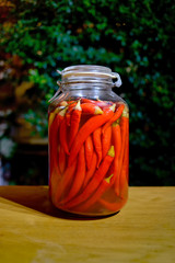 many homemade red chili hot peppers in big glass transparent cans