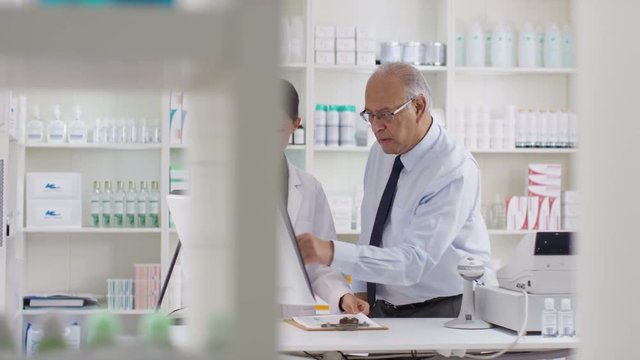  Workers in a chemist shop checking stock & discussing their work