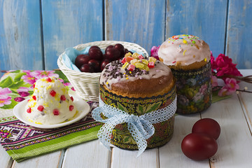 Traditional Easter cake with sugar glaze and candied fruit and red eggs in a white basket on a blue wooden background. The concept of Easter.